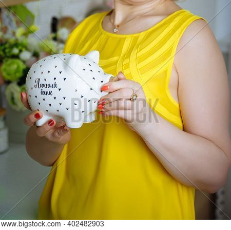 Torso Of A Woman In A Yellow T-shirt Holding A Porcelain Piggy Bank In The Form Of A Pig With An Ins