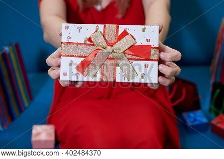 A Girl Giving A Gift Box Wit Red And Gold Bow.