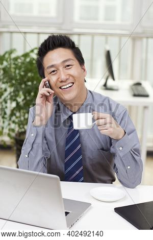 Businessman Using A Laptop And Phono In An Office High Quality Photo