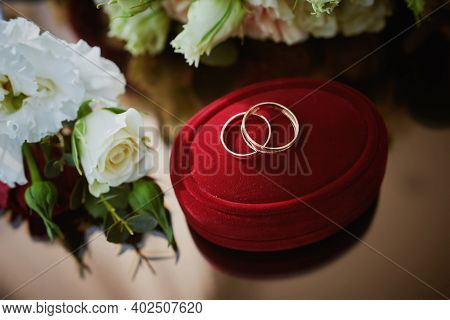 Close Up View Of Wedding Rings On A Red Velvet Box And Flowers On A Glass Table In The Hotel Room.
