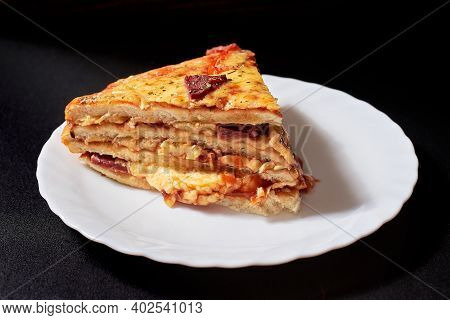 A Piece Of Italian Pizza Cake With Four Layers Full Of Grilled Salami, Ham And Moose Sausage. Black 