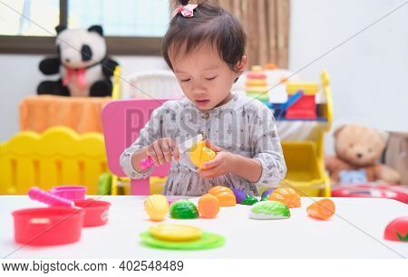 Cute Little Asian Toddler Baby Girl Child Having Fun Playing Alone With Cooking Toys, Slice And Play