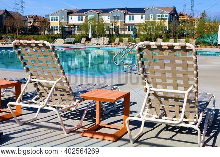 Modern Poolside Chairs Besides Small Outdoor Patio Tables Surrounding A Pool Taken In A Residential 