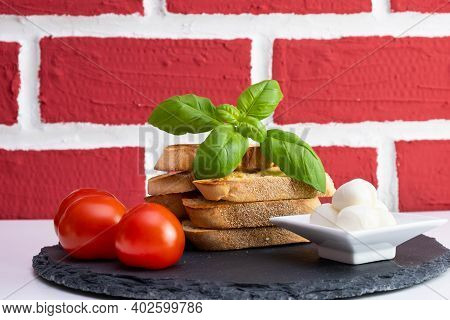 Basil, White Bread Croutons With Mozzarella And Tomatoes In A Cup On A Stone Stand On A Brick Backgr
