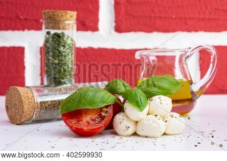 Mozzarella With Tomatoes And Basil On A White Table, Near Canola Oil In A Jug And Spices On A Brick 