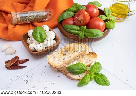 Fresh Tomatoes And Green Basil In A Wooden Bowl, Near Mozzarella, Croutons, Rapeseed Oil And Spices 