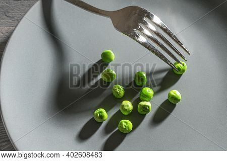 Some Green Peas And A Fork With Shadows On A Gray Plate, Meager Diet Meal After The Resolution To Sl