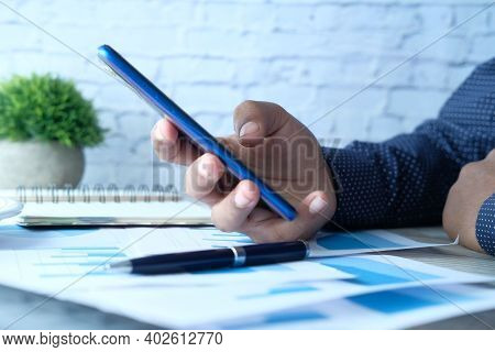 Side View Of Businessman Hand Using Smart Phone On Office Desk