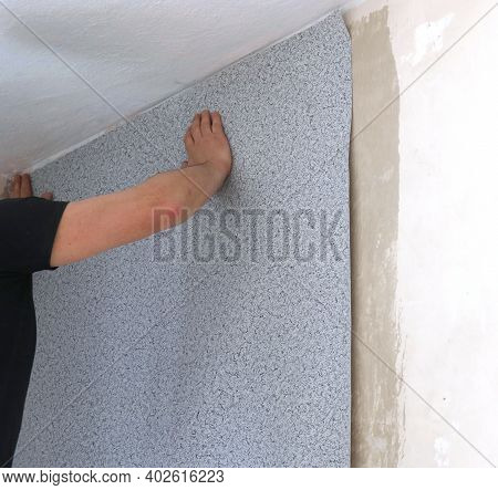 A Man In A Black T-shirt Gluing A Strip Of Gray Textured Wallpaper To The Wall Of A Room And Smoothi