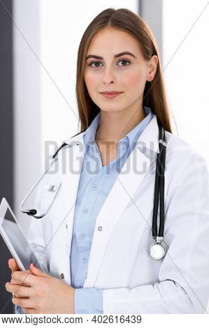 Doctor Woman Using Tablet Computer While Standing Straight Near Window In Hospital. Happy Physician 