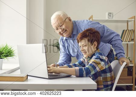 Happy Granddad Helps Grandson With Homework Or Asks Little Boy To Teach Him To Use Computer
