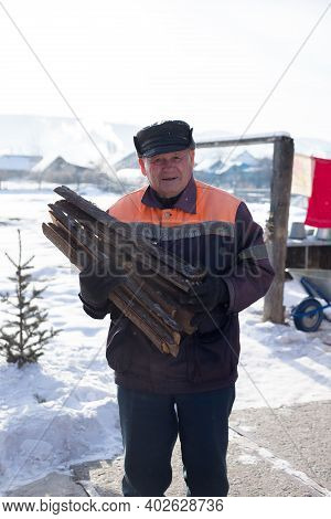 An Elderly Man Collects Firewood In A Russian Village In Winter