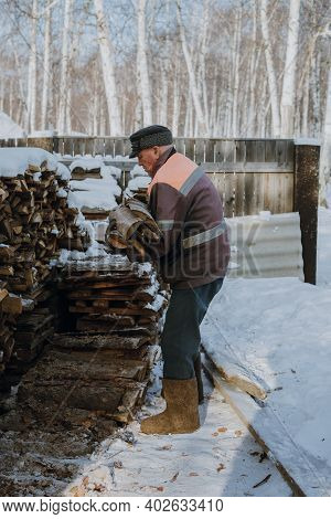 An Elderly Man Collects Firewood In A Russian Village In Winter