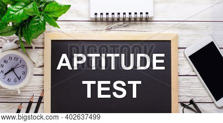Aptitude Test Written On A Black Background Near Pencils, A Smartphone, A White Notepad And A Green 