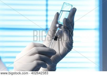 Woman Filling Syringe With Vaccine From Vial On Blurred Background, Closeup