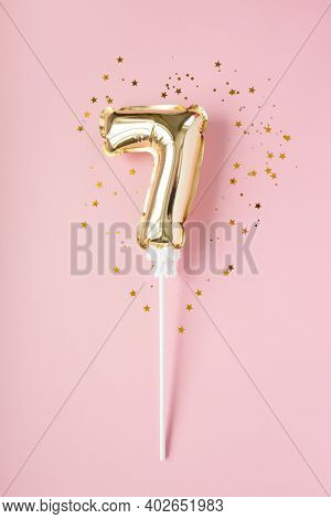 Gold Inflatable Number 7 On A Stick With Gold Confetti On A Pink Background.
