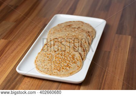 Derbyshire Oatcakes On A White Platter Viewed From An Angle With A Wooden Backdrop