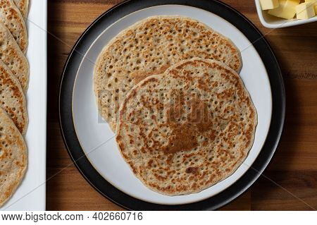 A Top Down View Of Derbyshire Oatcakes On A Black Rimmed Plate. A Stack Of Oatcakes And Butter Are A