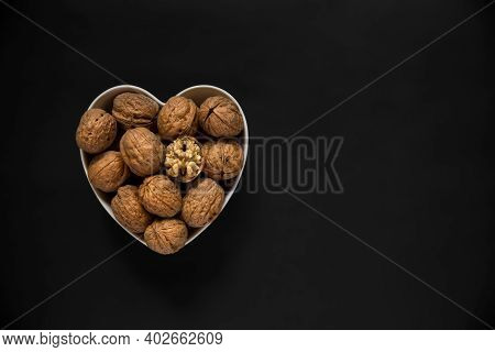 Whole Walnuts And One Cracked Broken Heart In A White Heart-shaped Bowl On A Black Background. Top V
