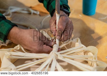 Close Up Of Mans Hands Tying The Loose Ends Of A Piece Of Leather Around A Wooden Support To Create 