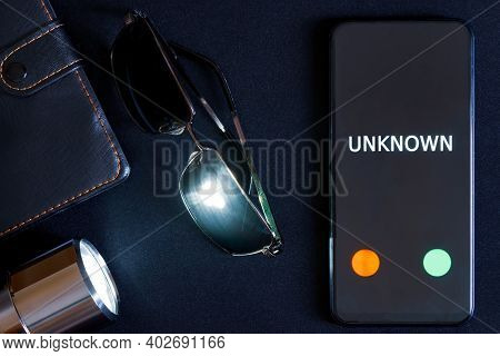 A Modern Smartphone With An Unknown Call, Sunglasses And A Flashlight Lie On A Black Surface. The Pr