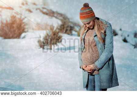 Nice Pregnant Woman Walking in the Countryside in Winter. Looking on the Tummy and Talking to the Baby. Happy Healthy Pregnancy.
