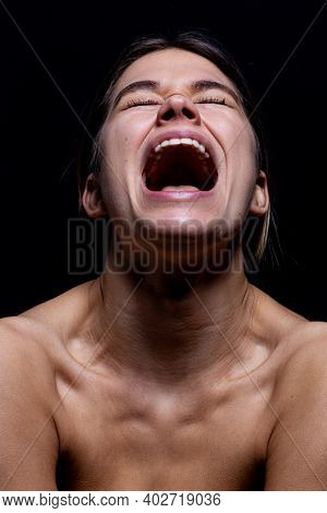 Screaming woman on a black background. Young woman's face with mouth open while screaming isolate from black. She is frustrated and in emotional pain. She is stresed and mad.