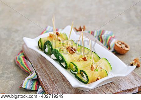 Roasted Zucchini Rolls Stuffed With Cream Cheese And Nuts On A White Plate On A Gray Concrete Backgr