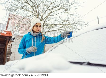 Woman scraping off ice from front window of her car in winter being a bit annoyed