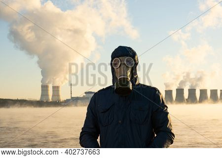 A Human In A Gas Mask Stands Against The Background Of A Nuclear Power Plant That Emits Chemicals In