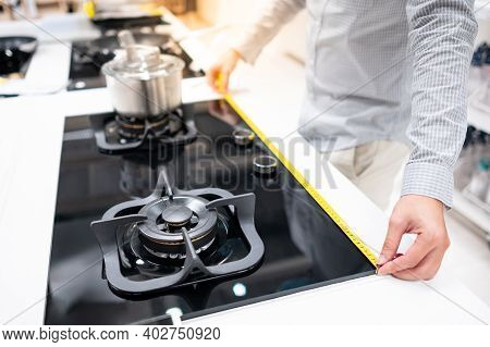 Male Hand Interior Designer Using Tape Measure On Gas Stove On Modern Countertop In Kitchen Showroom
