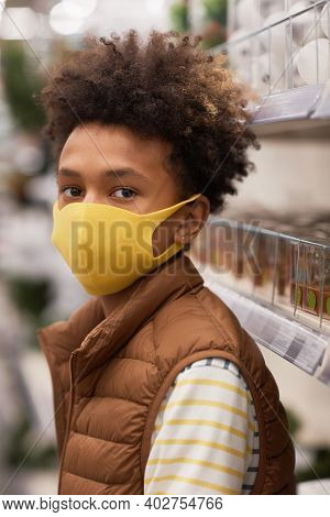Vertical Portrait Of Teenage African-american Boy Wearing Mask In Supermarket And Looking At Camera 