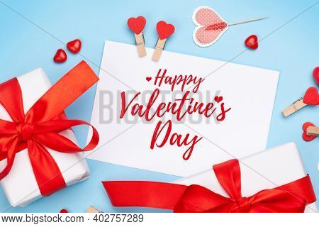 Valentines day greeting card. Gift boxes, heart decor and candy sweets over blue background. Top view flat lay