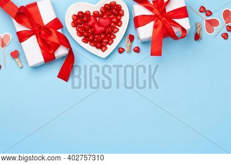 Valentines day greeting card template. Gift boxes, heart decor and candy sweets over blue background. Top view flat lay with copy space