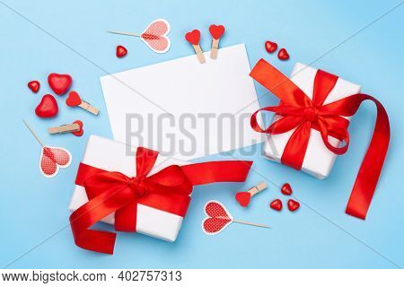 Valentines day greeting card template. Gift boxes, heart decor and candy sweets over blue background. Top view flat lay with copy space