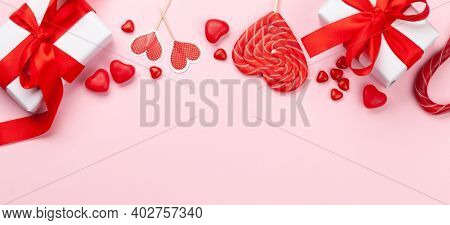 Valentines day greeting card template. Gift boxes, heart decor and candy sweets over pink background. Top view flat lay with copy space