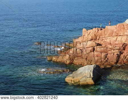 Red Rocks Called Rocce Rosse At Mediterranean Sea Coastline In Arbatax With Two Boys Fishing. Tortol