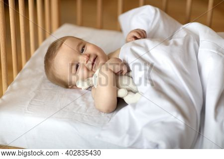 Adorable Smiling Blonde Baby Laying In Wooden Crib Under Blanket. Happy Little Kid Infant Woke Up Af