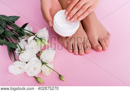 Partial View Of Barefoot Woman Holding Cosmetic Cream Near White Eustoma Flowers On Pink Background