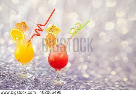 Two Glasses With Orange And Grapefruit Juice With Citrus Pieces, Ice, Straws And Cocktail Umbrellas