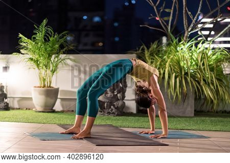 Asian female woman in sportswear bra pants practicing yoga during city lockdown alone in her apratment with background of cityscape illumination at night. Work out fitness healthy lifestyle concept.
