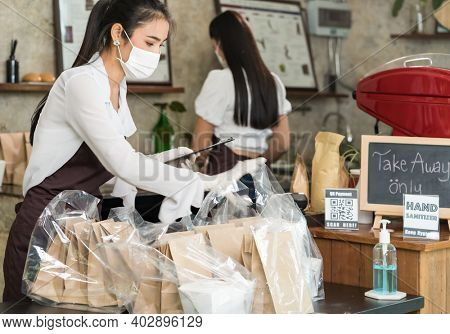 Asian waitress wear protective face mask prepare food for takeout and curbside pickup orders while city lockdown from coronavirus COVID-19 pandemic. This is essential service while lockdown.