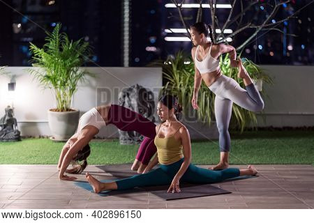 Group of asian women in sportswear pants practicing yoga during city lockdown in their apratment with distance in background of cityscape illumination night. Work out fitness healthy lifestyle concept