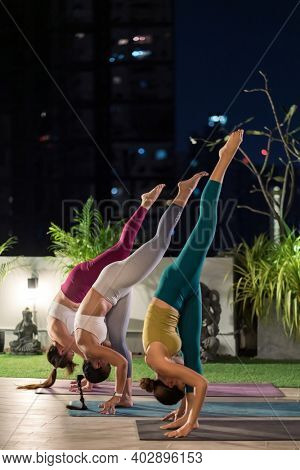 Group of asian women in sportswear pants practicing yoga during city lockdown in their apratment with distance in background of cityscape illumination night. Work out fitness healthy lifestyle concept