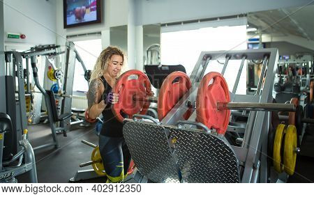 Woman With Long Curly Blonde Hair Holds A Heavy Barbell In His Hands. Bodybuilding, Trainer Of Fitne