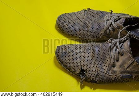 Old Torn Yellow Summer Shoes On A Yellow Background. A Pair Of Men's Heavily Worn Leather Shoes.