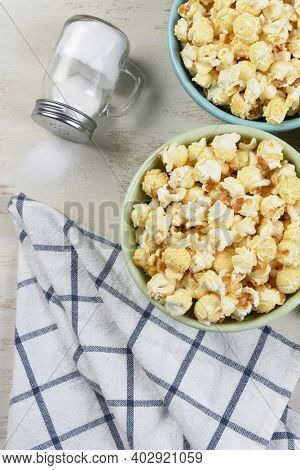 High angle shot of two different colored bowls of fresh popped popcorn with towl and salt shaker with salt spilling out. Vertical format.