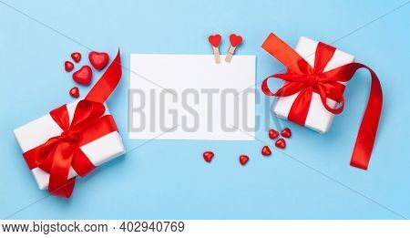 Valentines day greeting card template. Gift boxes, heart decor and candy sweets over blue background. Top view flat lay with copy space