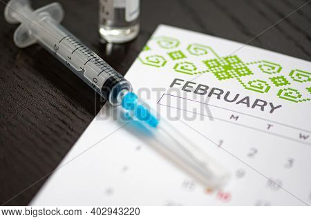 Syringe, Vial And Calendar With Month Of February On A Black Table Ready To Be Used. Covid Or Corona