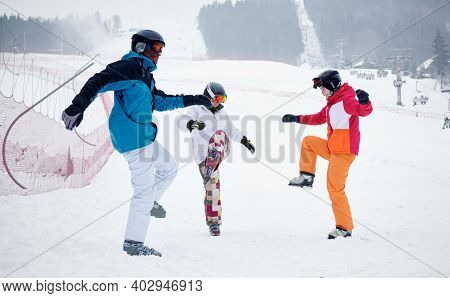 Group Of Friends Wearing Vivid Ski Suits Warming Up Before Skiing From Piste In Mountains In Winter.